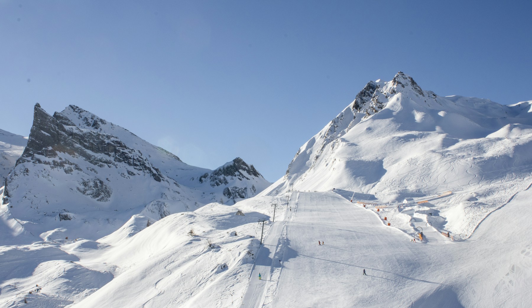 A broad white ski run and chairlift surrounded by snow-covered Alpine peaks